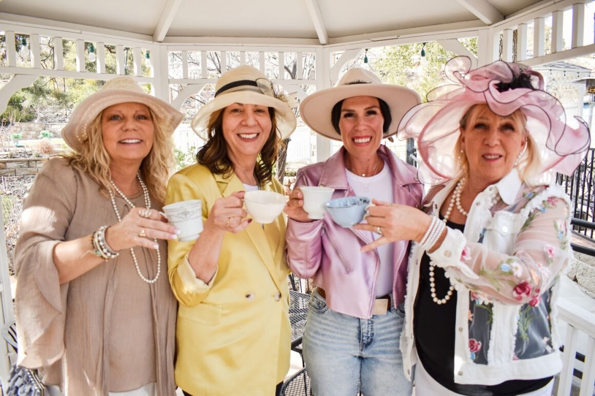 Four women in fancy hats raising teacups at a Willow Creek Inn tea party.